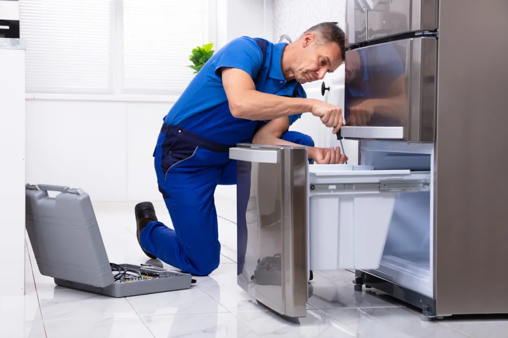 Technician repairing a refrigerator in a customer's kitchen